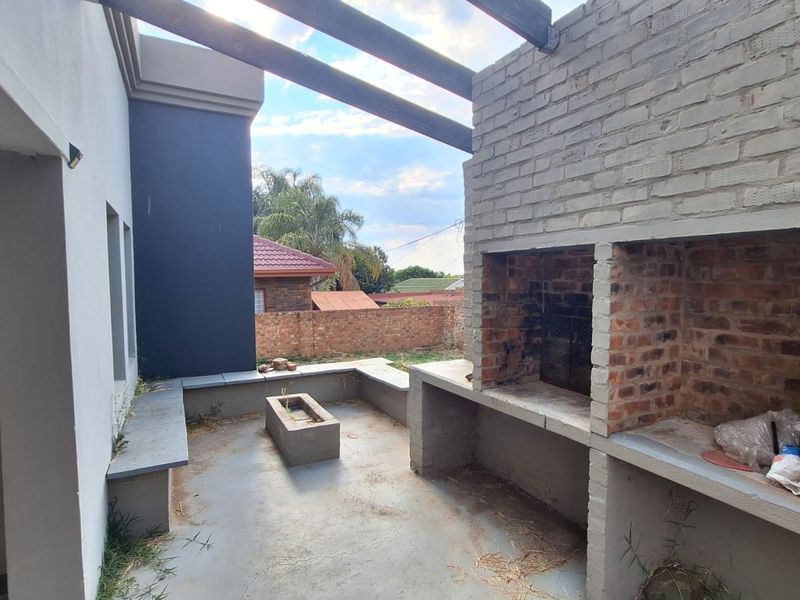 Outdoor patio area featuring a built-in brick braai, concrete bench seating, and timber pergola beams, offering a functional space for outdoor entertaining.