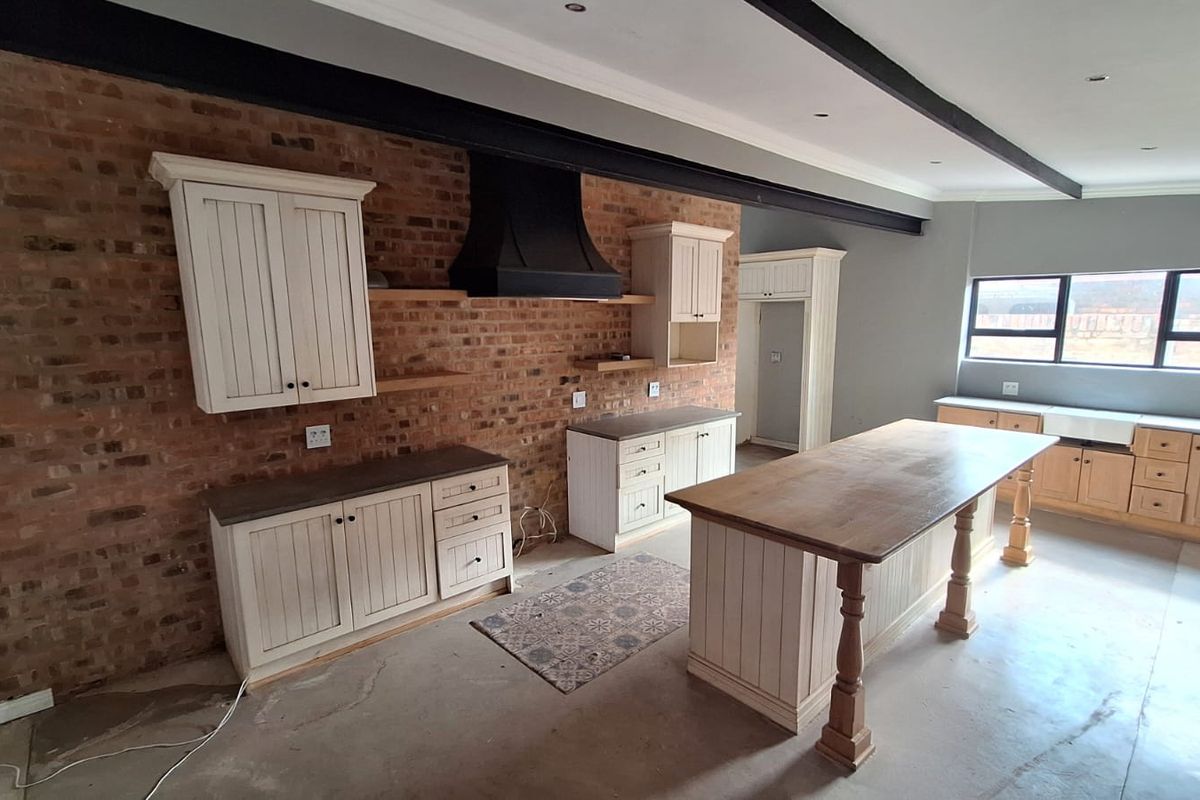 Spacious kitchen featuring exposed brick walls, custom cabinetry, a large central island, and exposed ceiling beams, currently awaiting final flooring and finishing touches.