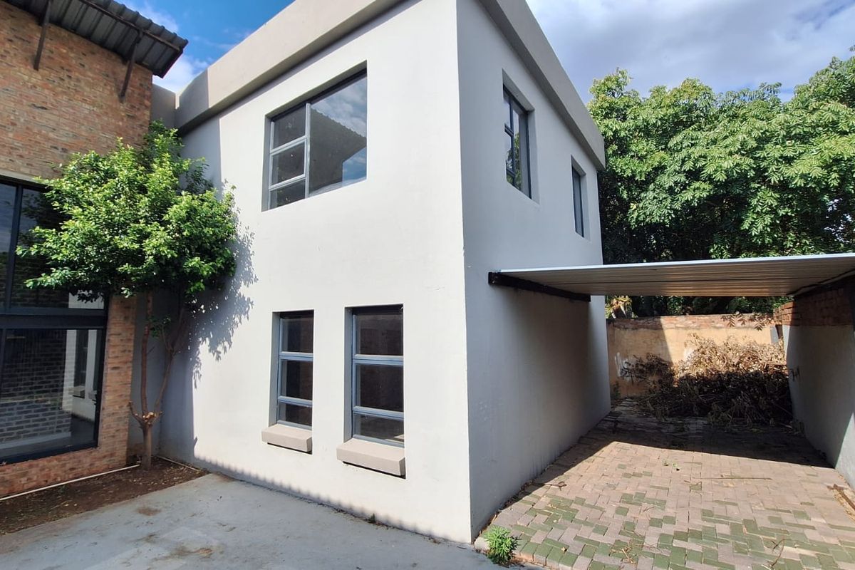 Rear exterior view of the property featuring a paved carport, modern aluminium window frames, and a combination of plastered and exposed brick wall finishes.
