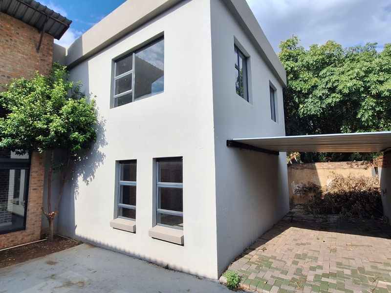 Rear exterior view of the property featuring a paved carport, modern aluminium window frames, and a combination of plastered and exposed brick wall finishes.