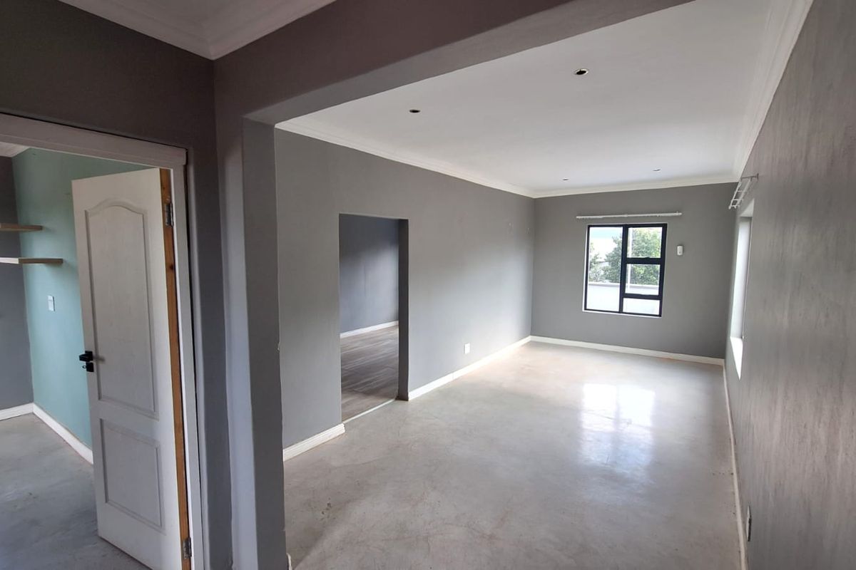 A bright, empty living area featuring polished concrete floors, neutral grey walls, and recessed lighting, offering a clean and modern blank canvas.