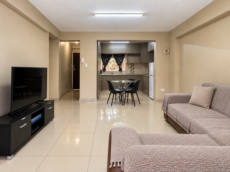 Open-plan living and kitchen area featuring neutral tiled flooring, built-in cabinetry, and a functional layout connecting the lounge to the kitchen space.