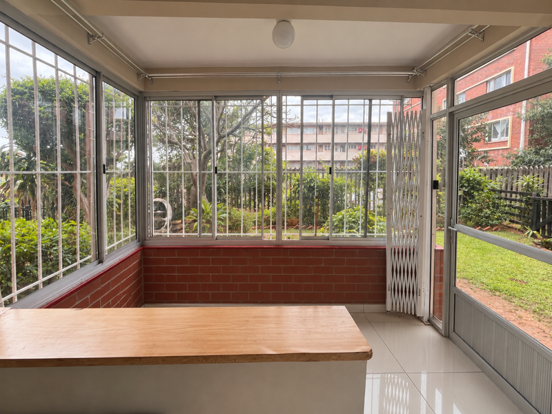 Enclosed patio area featuring large sliding windows with security bars, brick base detailing, and direct access to the garden through a glass door.