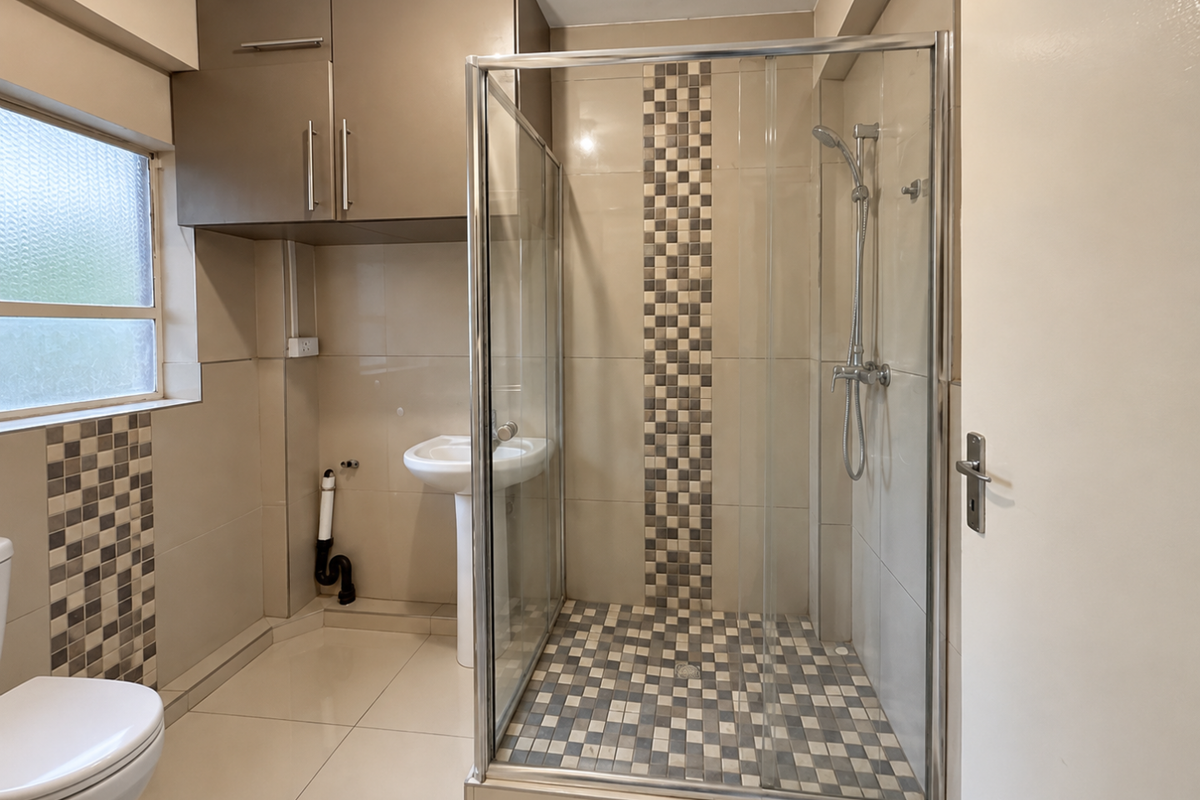 A functional bathroom featuring a glass-enclosed shower, pedestal basin, and wall-mounted storage cabinetry with neutral tiled finishes.