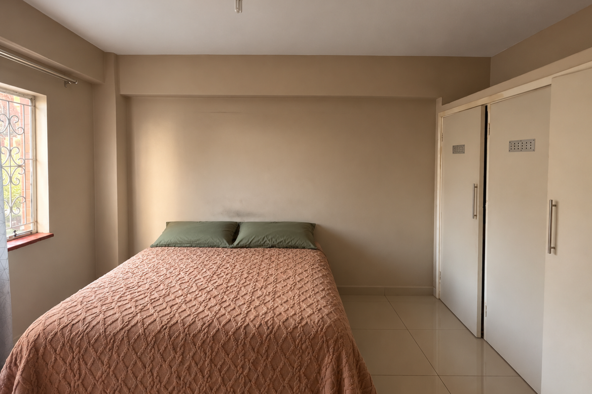 A bedroom featuring neutral wall tones, tiled flooring, and built-in cupboards, offering a functional space with natural light from the side window.