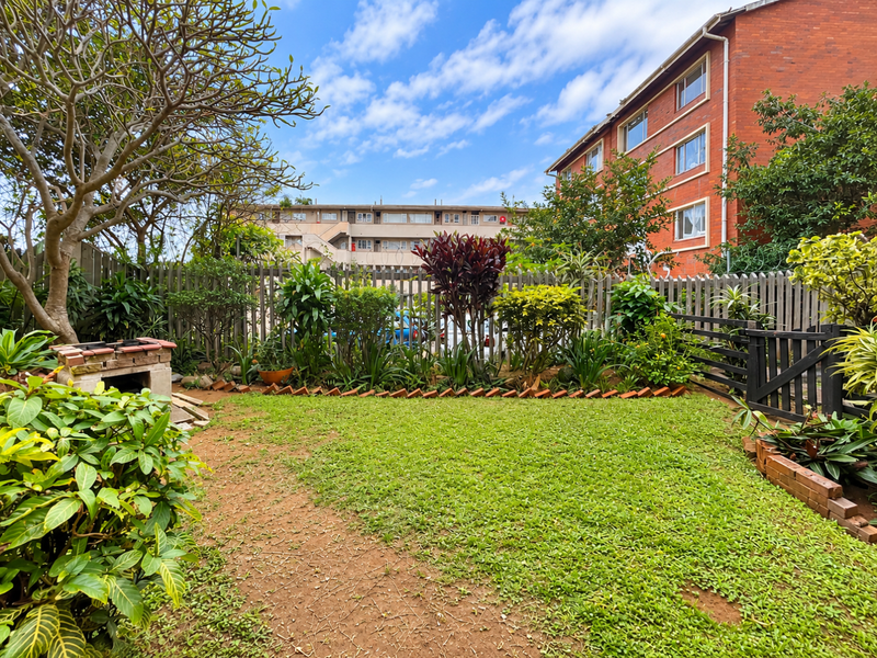 A private garden area featuring a built-in brick braai, established landscaping, and timber fencing, offering a functional outdoor space for the apartment.