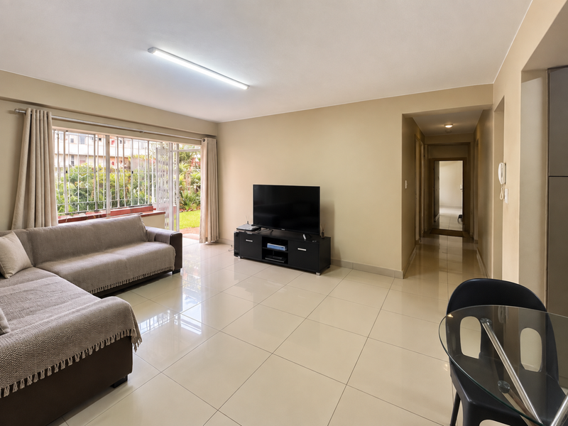 Spacious living area featuring large format floor tiles, a sliding door with security gate leading to the garden, and an integrated intercom system.