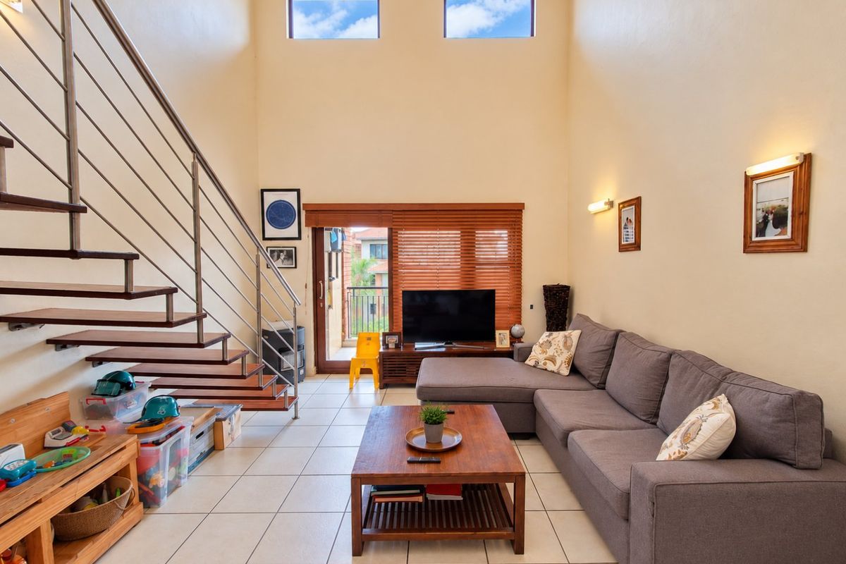 Spacious living room featuring high ceilings, tiled flooring, a modern staircase with metal railings, and large windows providing ample natural light.