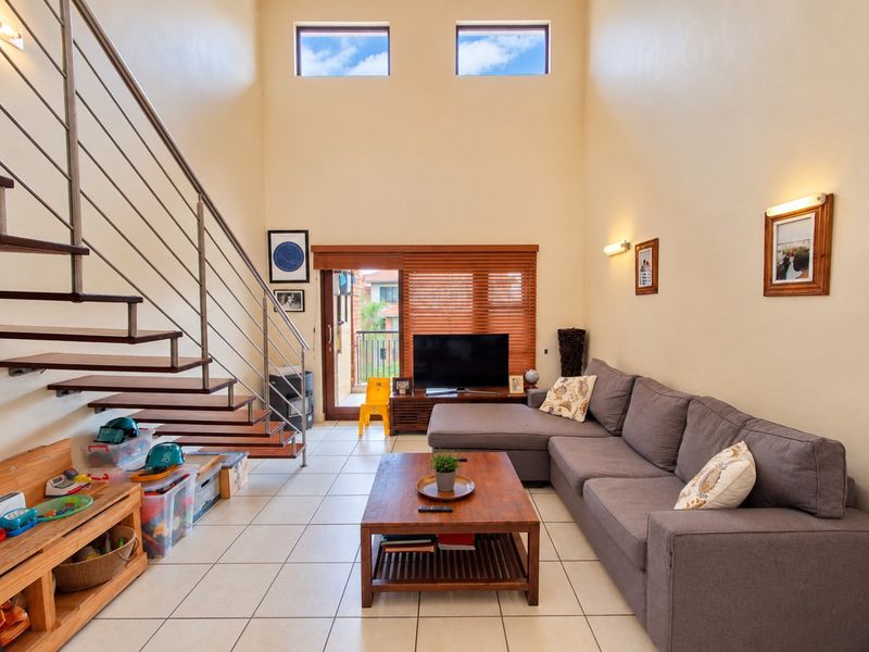 Spacious living room featuring high ceilings, tiled flooring, a modern staircase with metal railings, and large windows providing ample natural light.