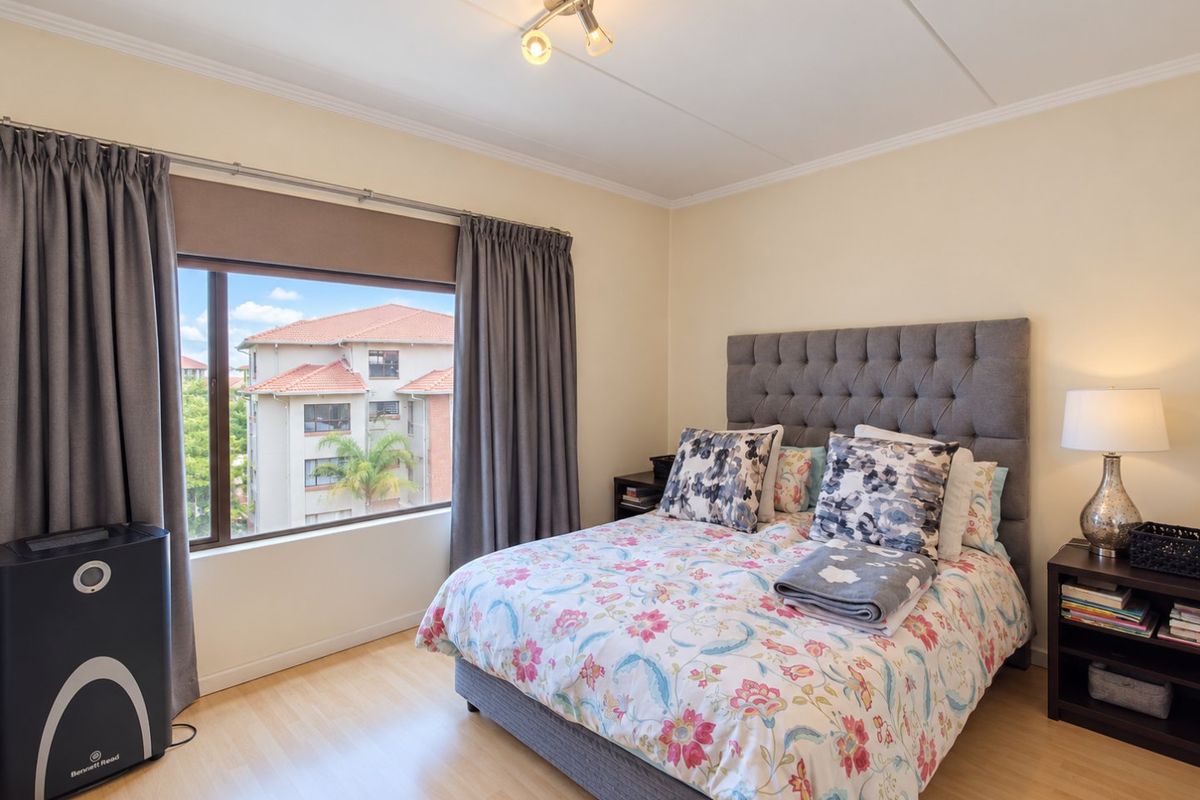 A well-maintained bedroom featuring laminate flooring, neutral wall tones, and a large window providing natural light and views of the surrounding apartment complex.