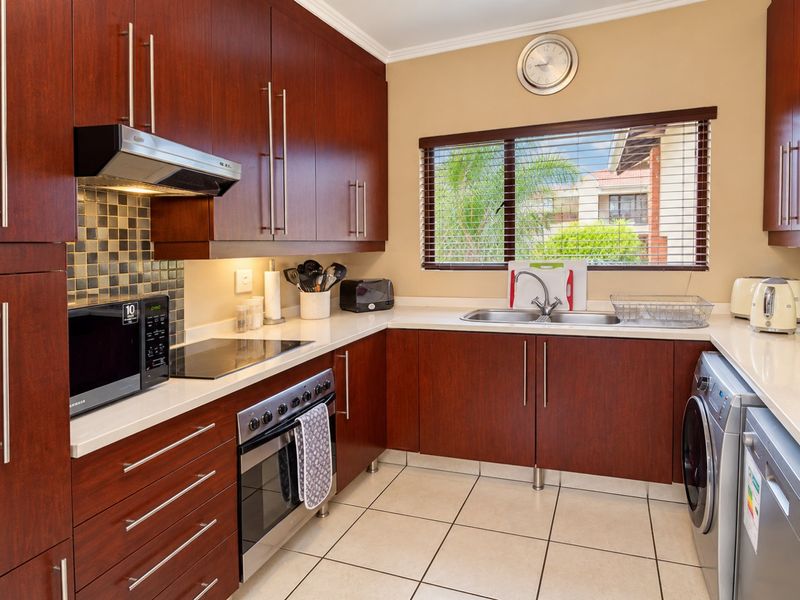A well-maintained kitchen featuring dark wood cabinetry, stone countertops, a mosaic backsplash, and integrated appliances, offering a functional and classic workspace.