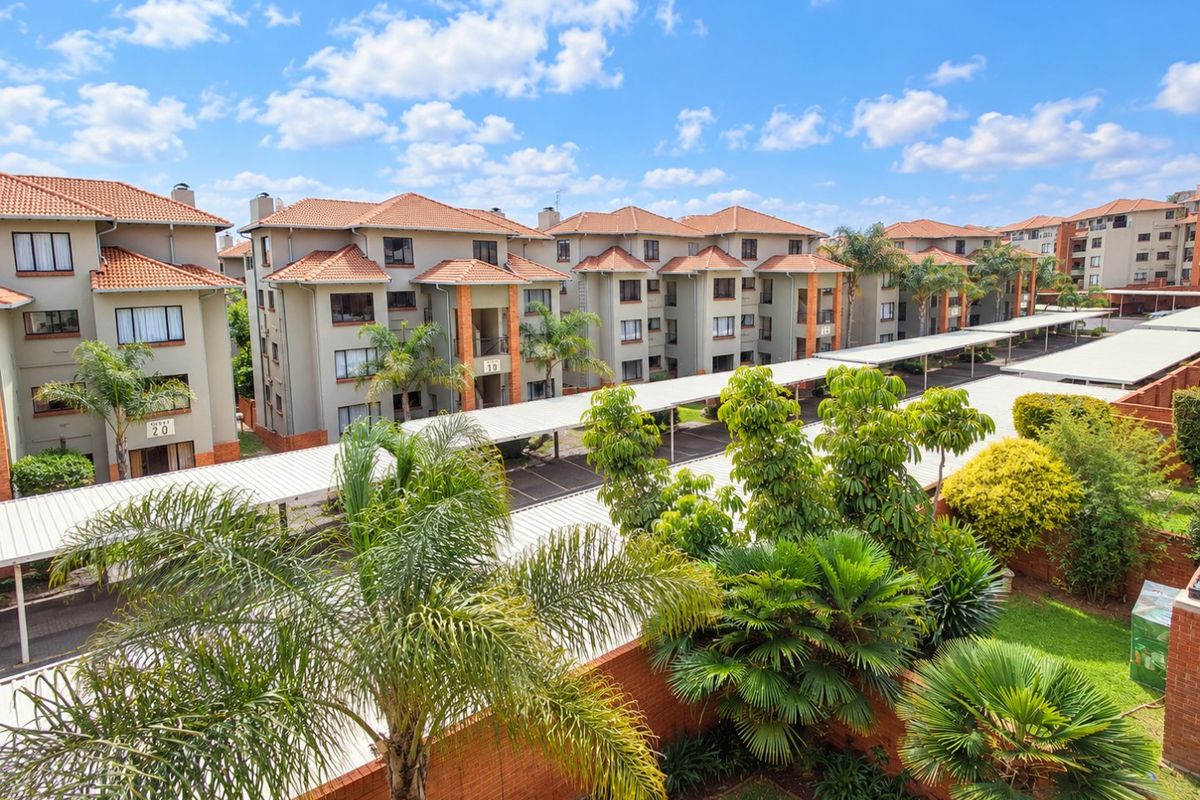 An elevated view of an apartment complex featuring multiple residential blocks, covered parking structures, and well-maintained communal garden areas.