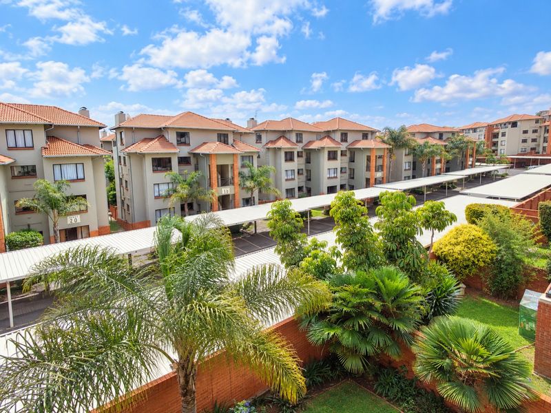 An elevated view of an apartment complex featuring multiple residential blocks, covered parking structures, and well-maintained communal garden areas.