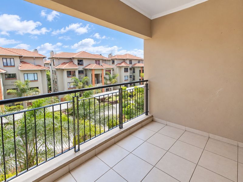 A clean, covered balcony featuring tiled flooring and a metal balustrade, offering an elevated view of the surrounding apartment complex.