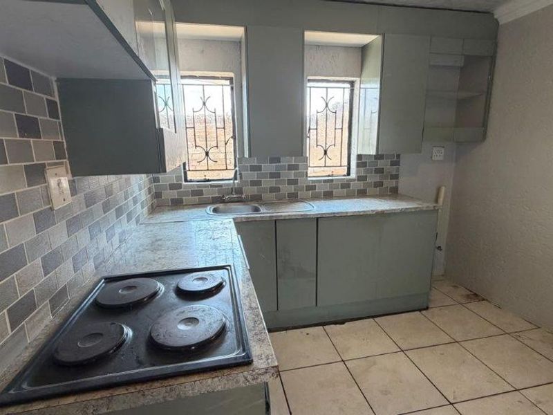 A functional kitchen featuring built-in cabinetry, laminate countertops, a stainless steel sink, and an electric hob with a tiled backsplash.
