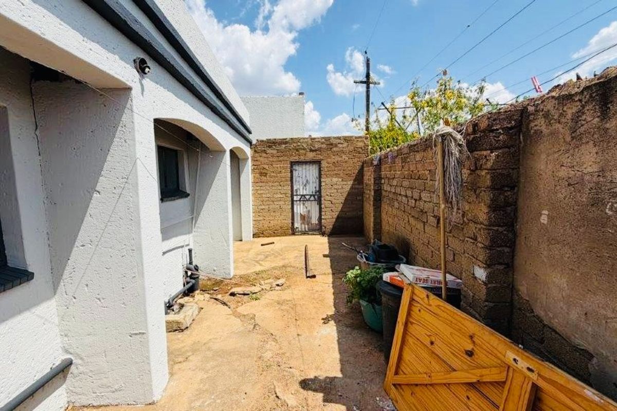 Rear exterior area featuring a paved courtyard, brick boundary wall, and access to a secondary metal door.