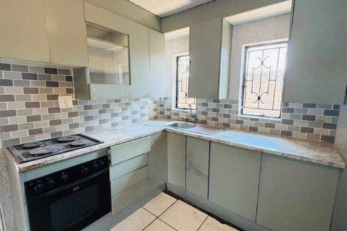 A compact kitchen featuring built-in cabinetry, a tiled backsplash, an integrated oven and hob, and stainless steel sink with security-barred windows.
