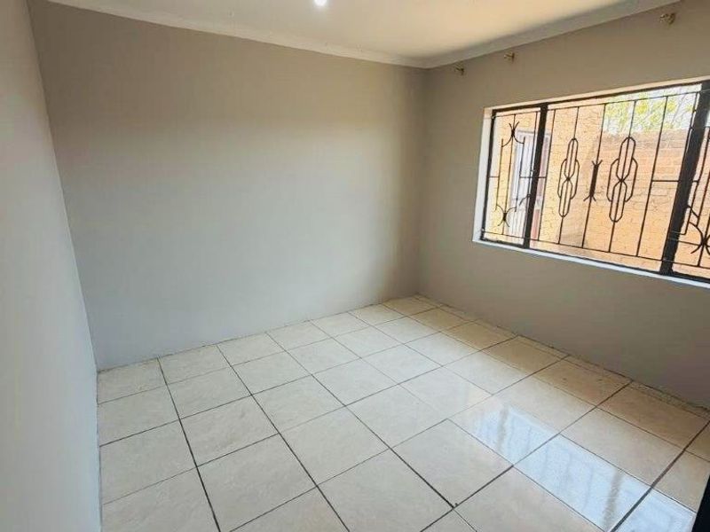 A clean, empty bedroom featuring neutral wall paint, tiled flooring, and a window fitted with security bars.
