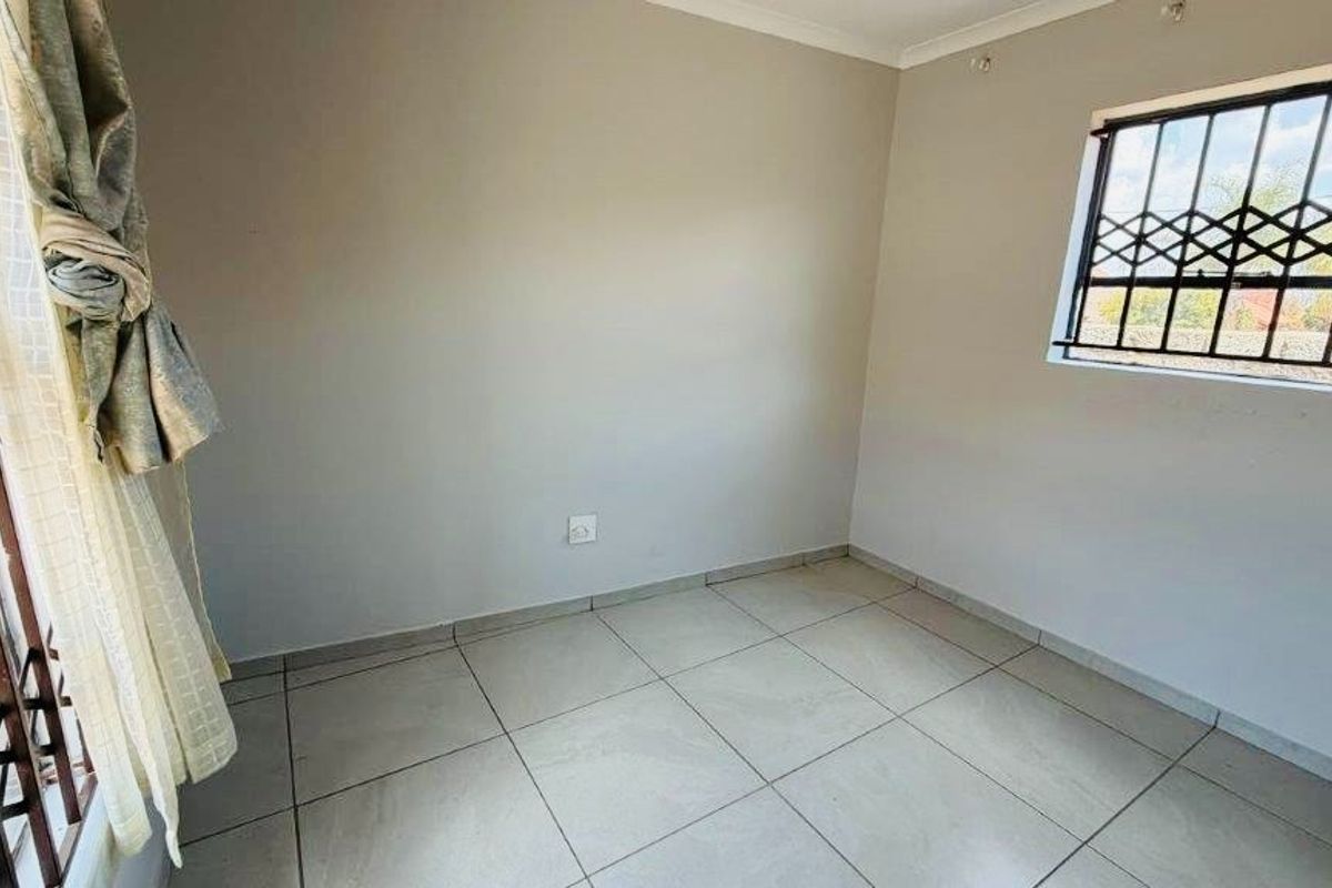 A clean, empty bedroom featuring neutral tiled flooring and windows fitted with security bars.
