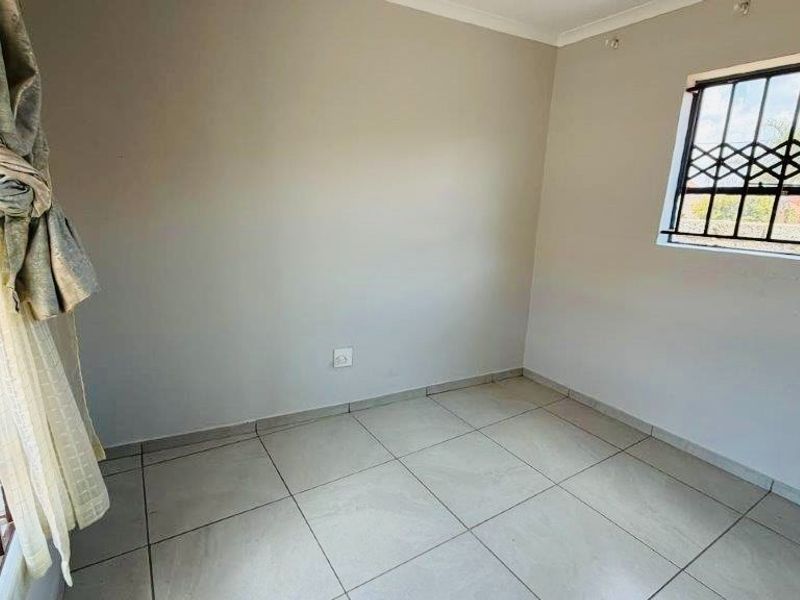 A clean, empty bedroom featuring neutral tiled flooring and windows fitted with security bars.