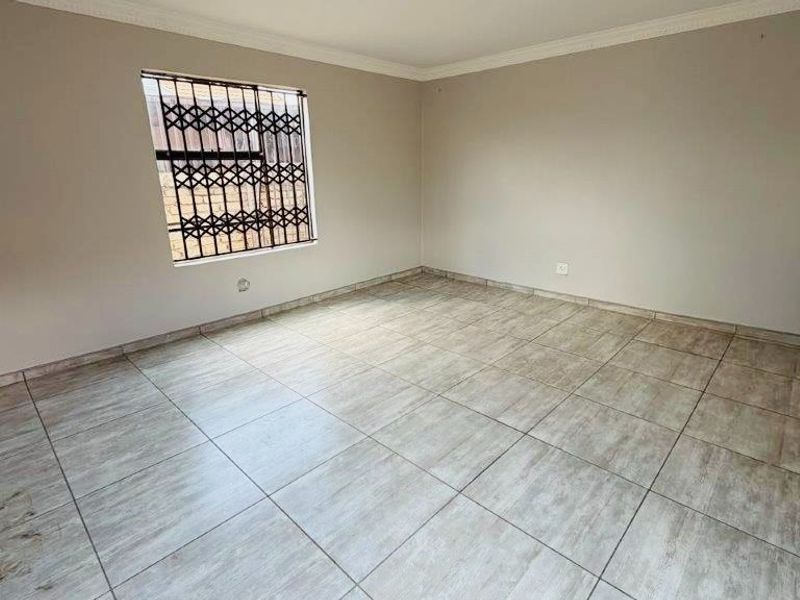 An empty living room featuring neutral wall paint, tiled flooring, and security fixtures on the window and entrance.