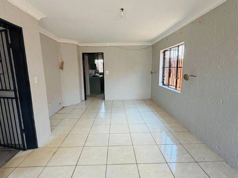 An empty living room featuring tiled flooring, security gate, and burglar bars, presenting a blank canvas for renovation and interior design updates.