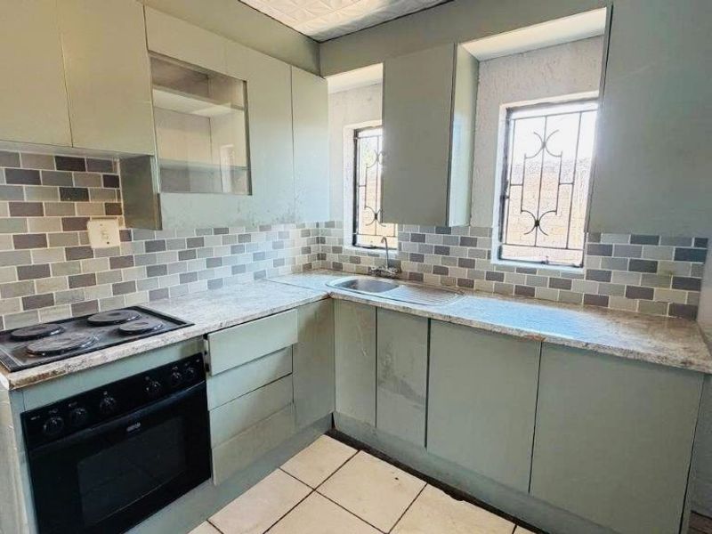 A functional kitchen featuring built-in cabinetry, a tiled backsplash, integrated oven and hob, and stainless steel sink with security-barred windows.