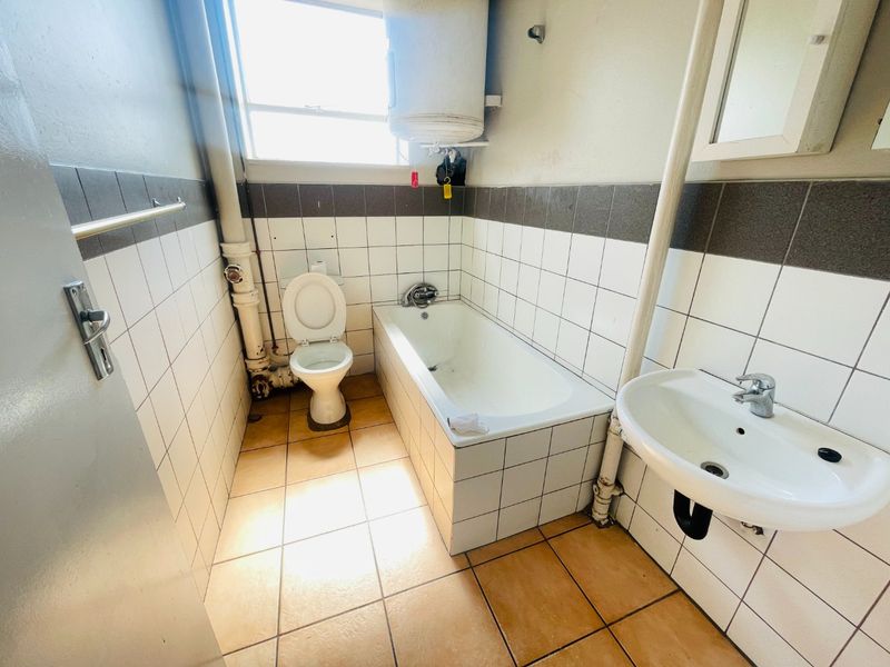 A functional bathroom featuring a bathtub, toilet, and wall-mounted basin with tiled finishes and exposed plumbing.