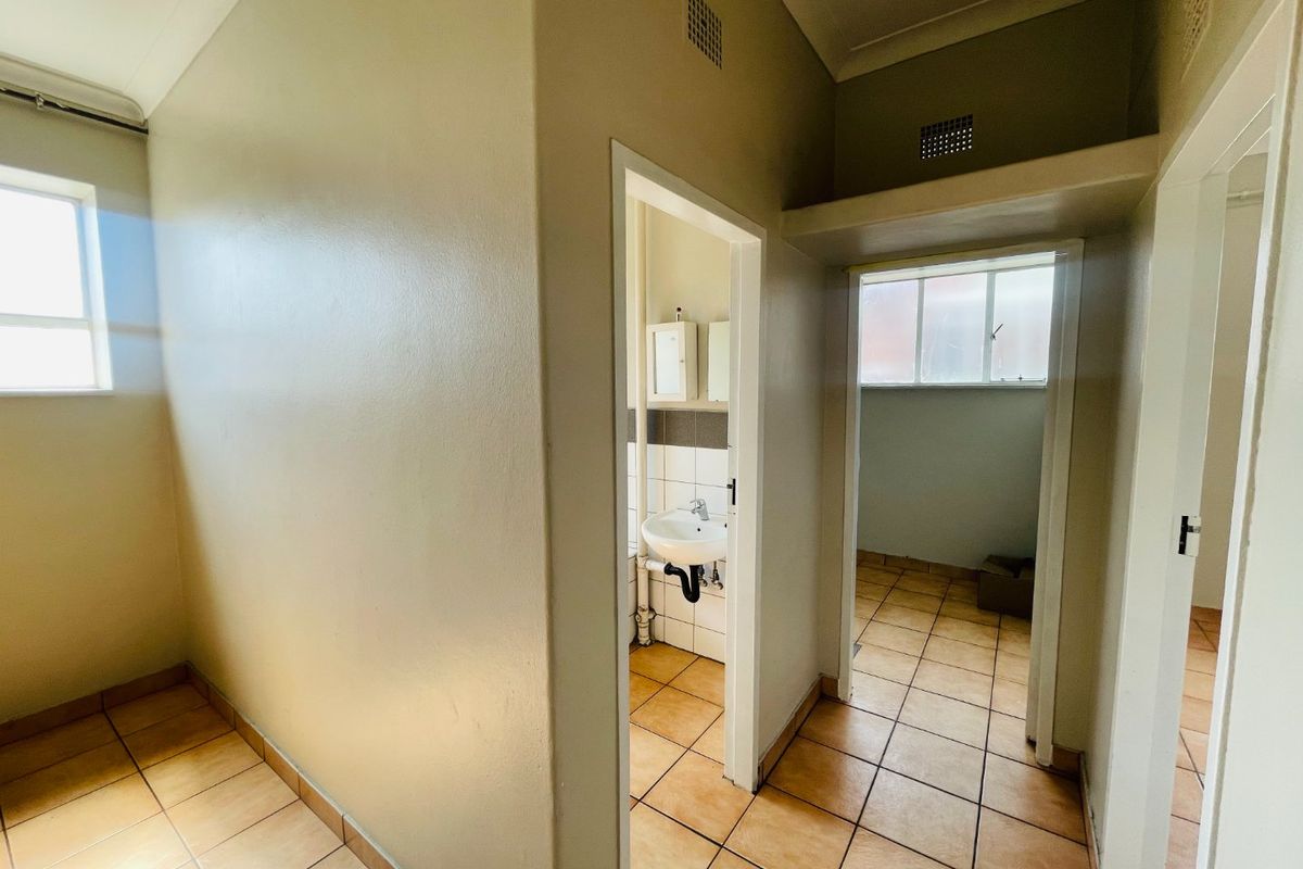 A functional hallway area featuring tiled flooring and access to adjacent rooms, including a small wash area with a basin.