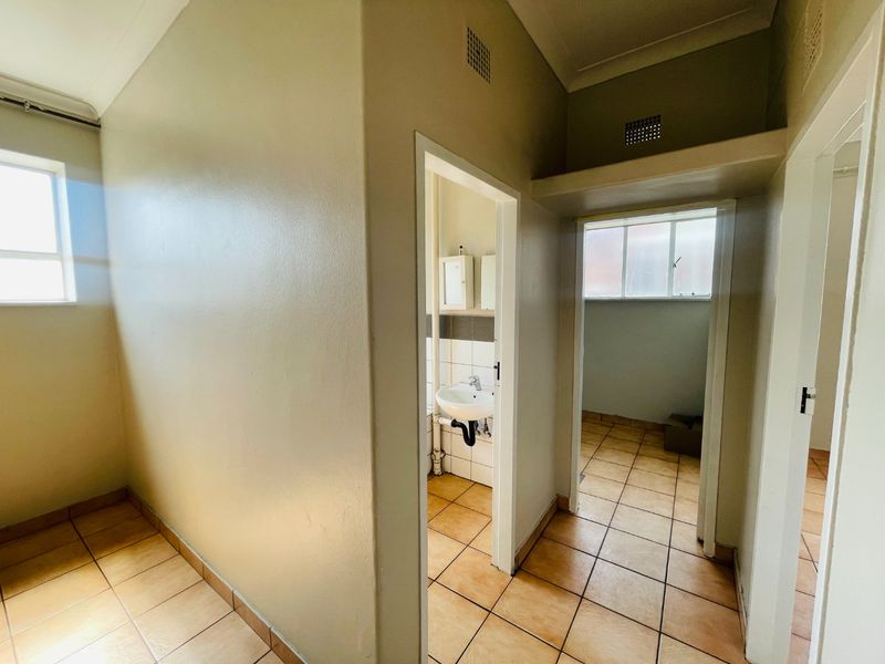 A functional hallway area featuring tiled flooring and access to adjacent rooms, including a small wash area with a basin.