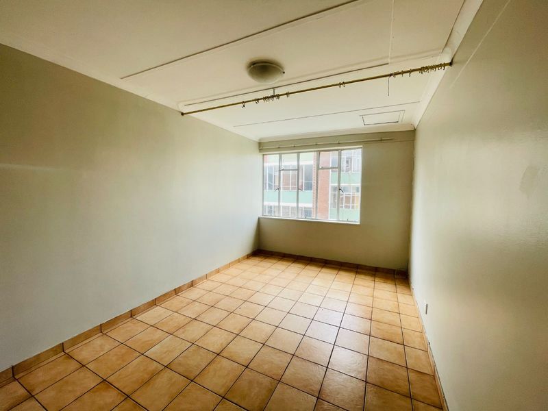 An empty bedroom featuring tiled flooring, a metal-framed window, and a ceiling-mounted light fixture, offering a blank canvas for renovation.