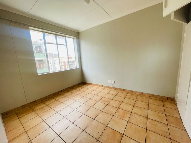 An empty bedroom featuring tiled flooring and a large window, providing a blank canvas for potential interior design updates.