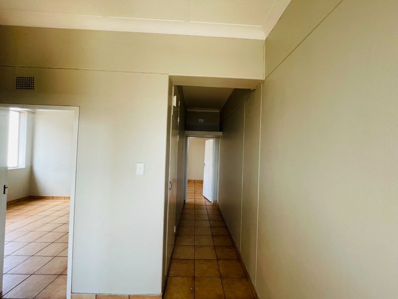 A vacant hallway featuring ceramic floor tiles and coved ceiling cornices, providing access to adjacent rooms within the apartment.
