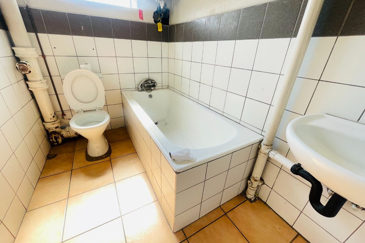 A functional bathroom featuring a bathtub, toilet, and wall-mounted basin with exposed plumbing and tiled finishes throughout.