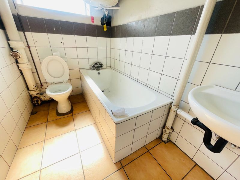 A functional bathroom featuring a bathtub, toilet, and wall-mounted basin with exposed plumbing and tiled finishes throughout.