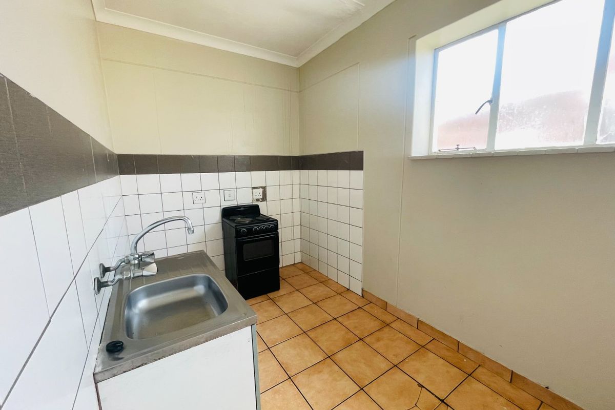 A compact kitchen featuring tiled flooring, a stainless steel sink, and a freestanding stove, offering a functional space ready for modernization.