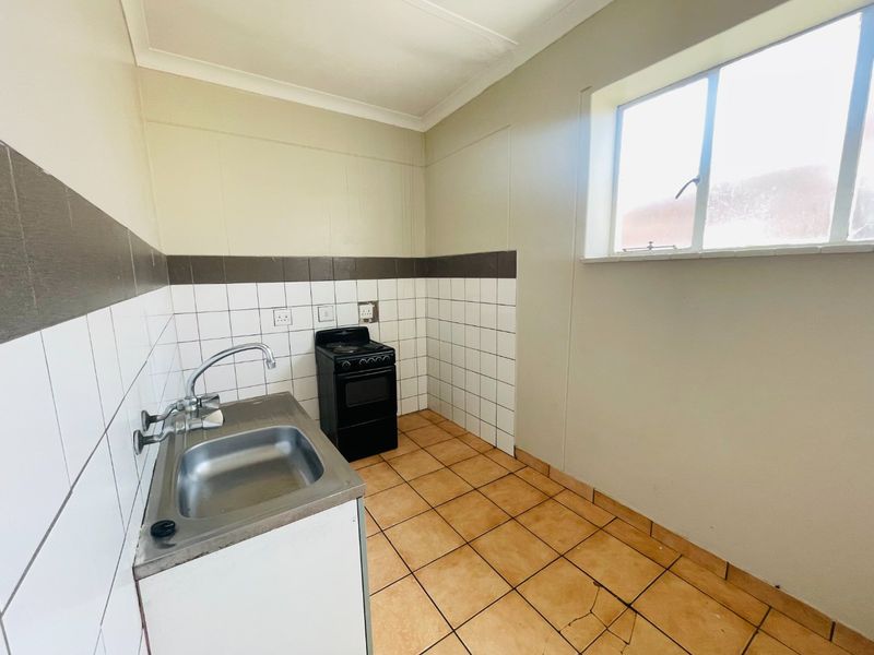A compact kitchen featuring tiled flooring, a stainless steel sink, and a freestanding stove, offering a functional space ready for modernization.