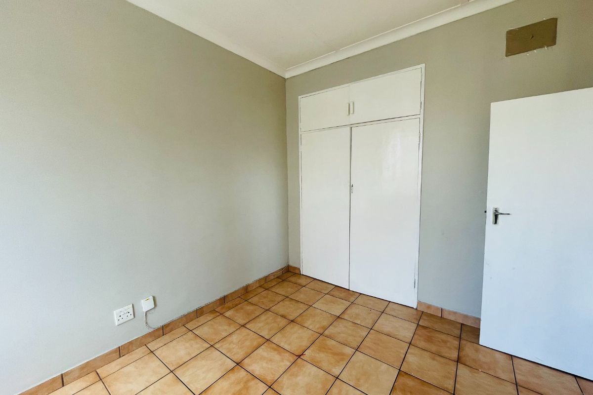 An empty bedroom featuring tiled flooring, built-in cupboards, and neutral wall finishes, providing a blank canvas for personalization.