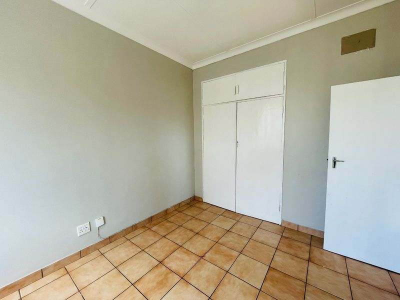 An empty bedroom featuring tiled flooring, built-in cupboards, and neutral wall finishes, providing a blank canvas for personalization.