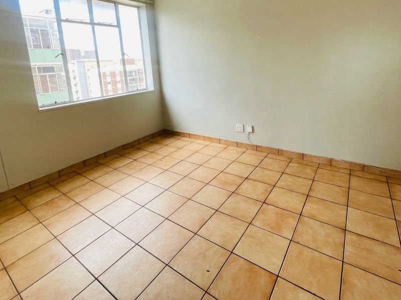An empty bedroom featuring tiled flooring and a large window, providing a blank canvas for personalization and interior design updates.