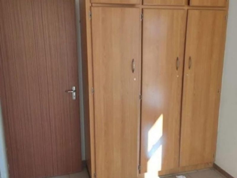 A bedroom featuring built-in wooden cupboards and tiled flooring, offering a clean and functional space ready for personalization.