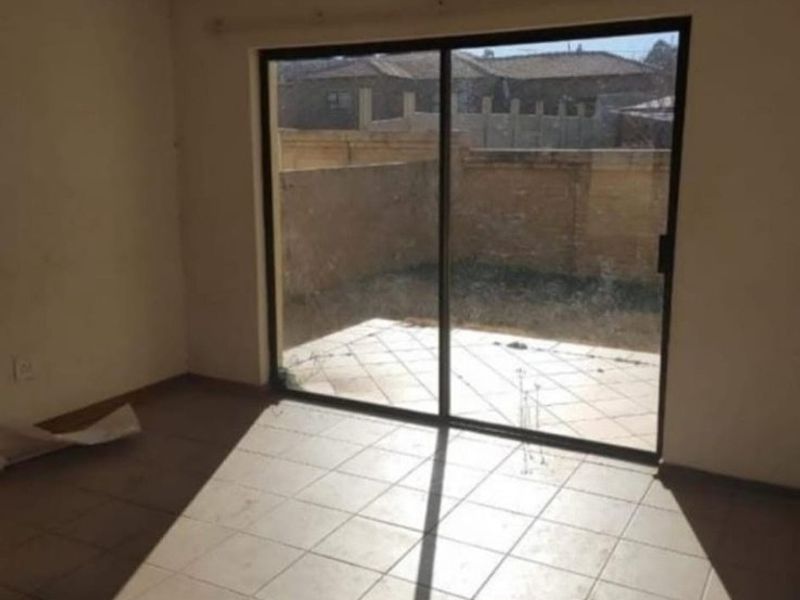 An empty living room featuring tiled flooring and a large sliding glass door providing access to an outdoor patio area.