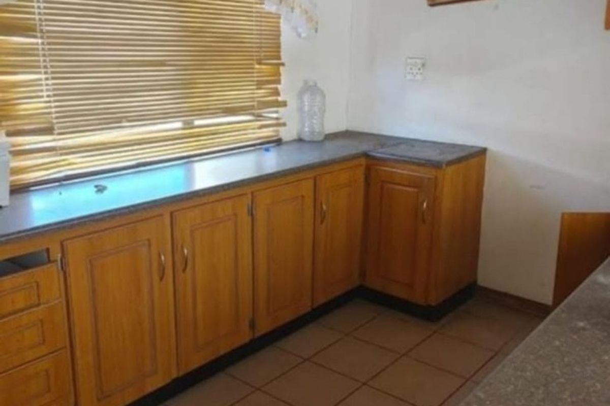 A dated kitchen featuring wooden cabinetry, laminate countertops, and ceramic floor tiles, offering a functional layout ready for modernization.