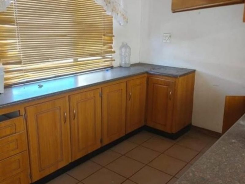 A dated kitchen featuring wooden cabinetry, laminate countertops, and ceramic floor tiles, offering a functional layout ready for modernization.