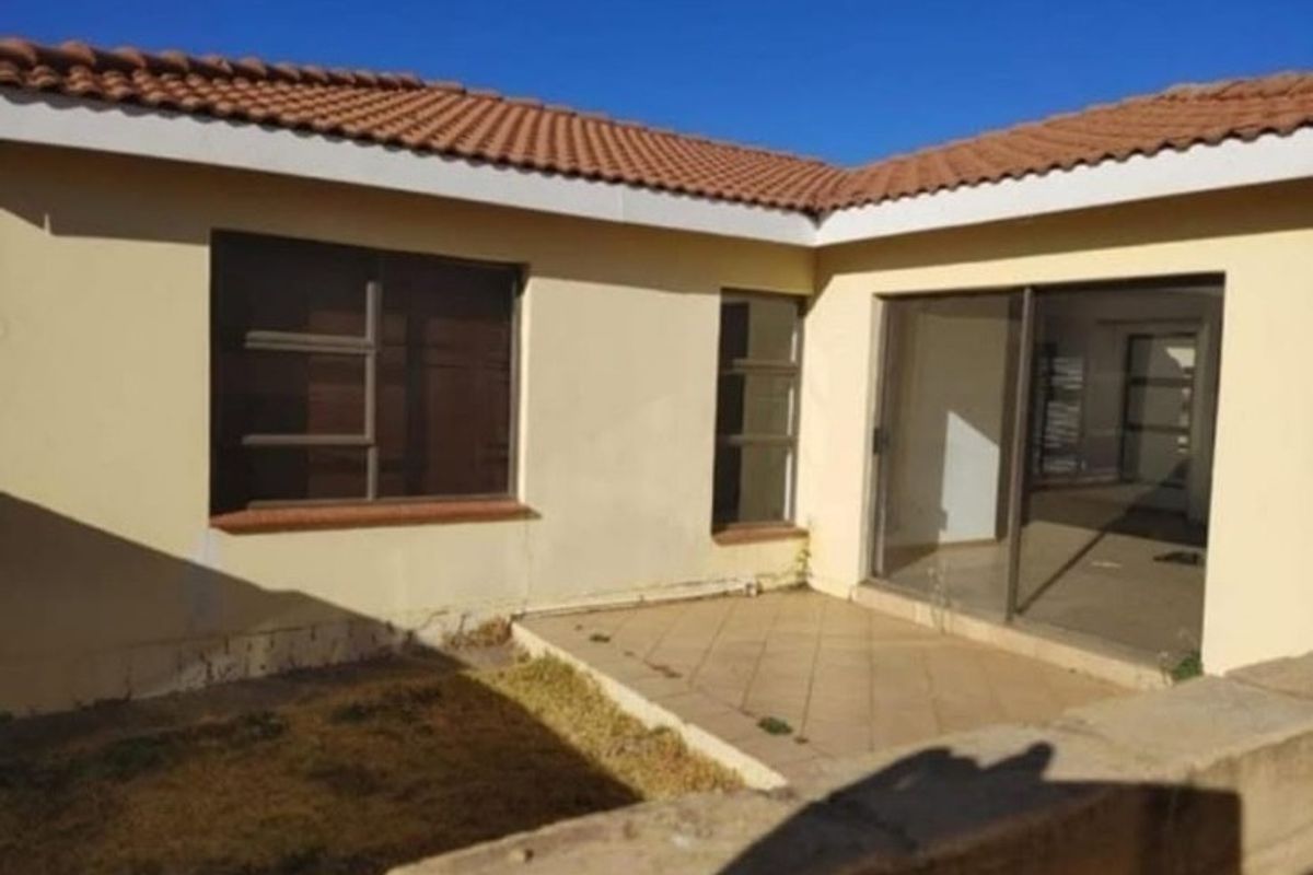 Rear view of the apartment featuring a tiled patio, sliding glass doors, and a tiled roof, showing signs of wear and maintenance needs.