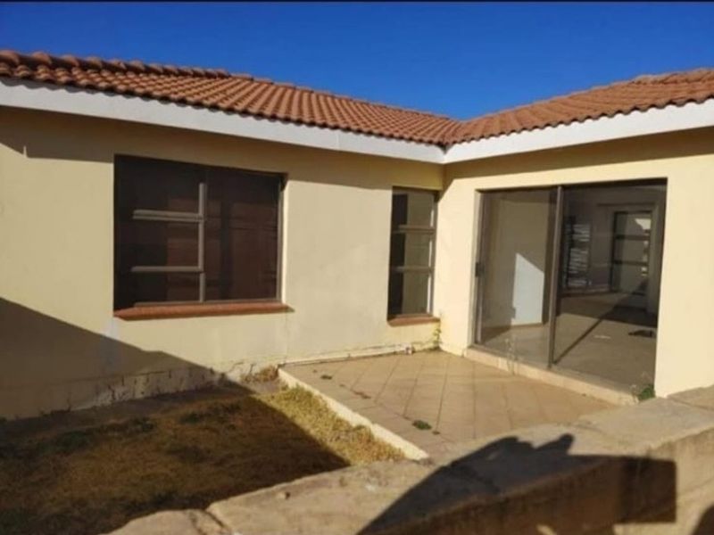 Rear view of the apartment featuring a tiled patio, sliding glass doors, and a tiled roof, showing signs of wear and maintenance needs.
