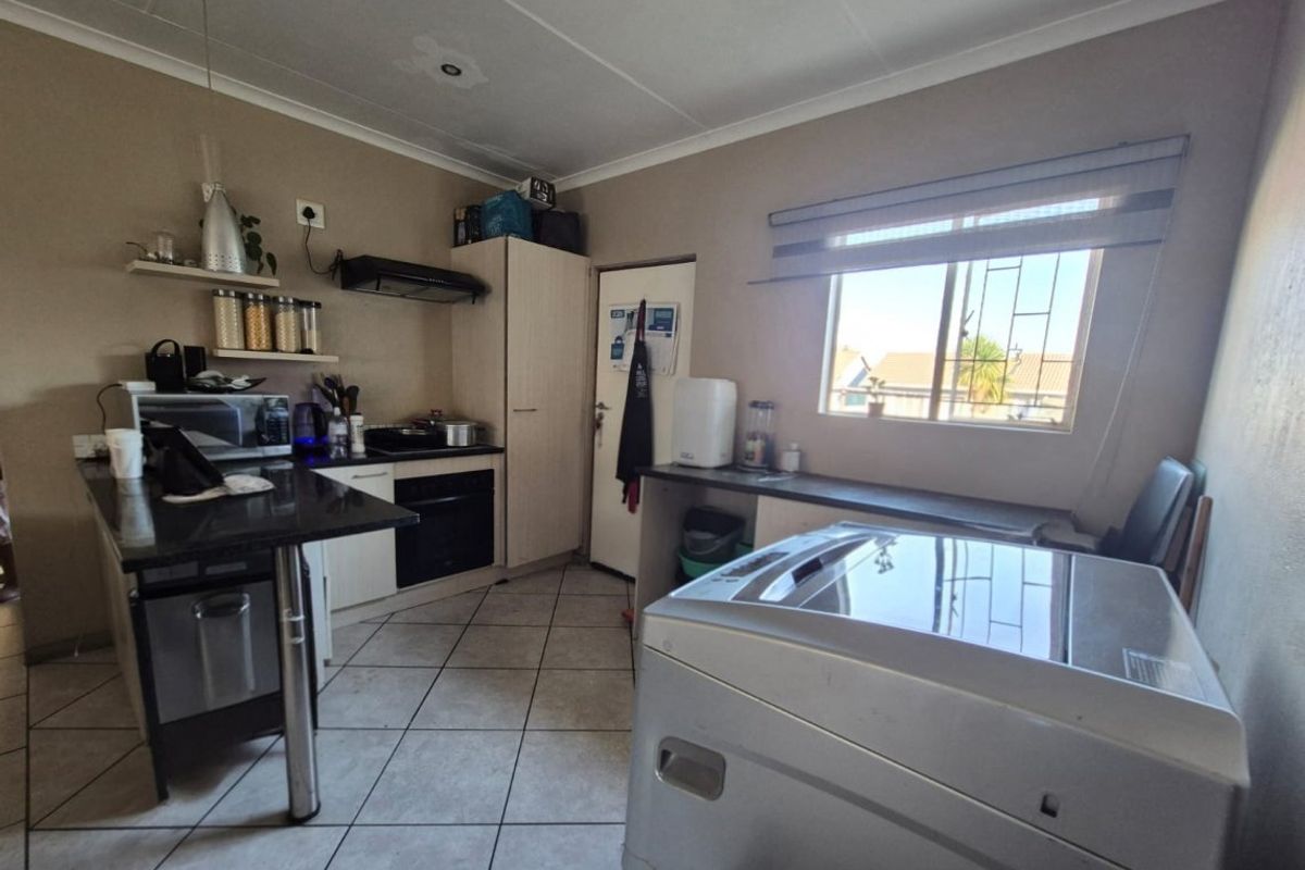 Functional kitchen featuring built-in oven, extractor fan, granite countertops, and tiled flooring, with a window providing natural light and security bars.