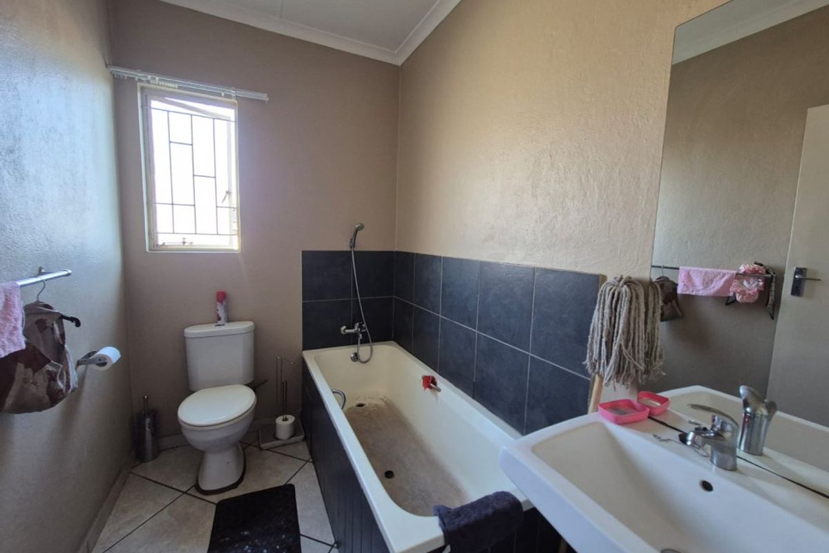 A functional bathroom featuring a bathtub with tiled splashback, pedestal basin, and toilet, requiring cosmetic updates to improve its overall condition.