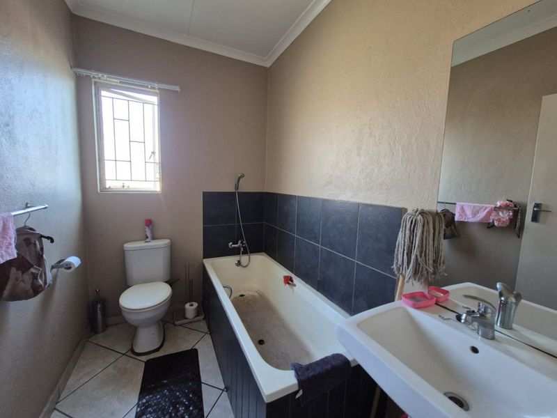 A functional bathroom featuring a bathtub with tiled splashback, pedestal basin, and toilet, requiring cosmetic updates to improve its overall condition.