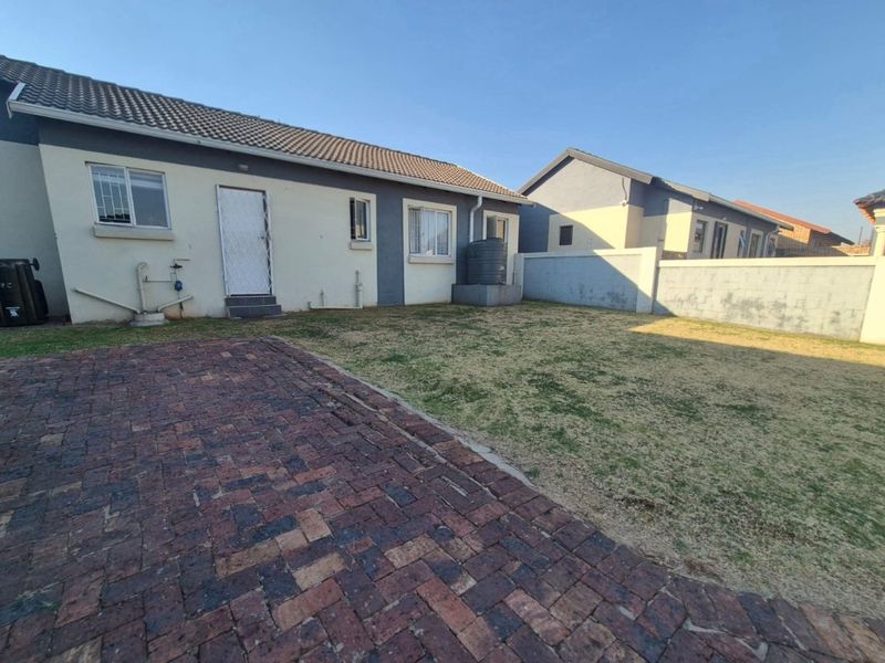 Rear view of the property featuring a brick paved patio, a small lawn area, and a perimeter wall with a water storage tank.